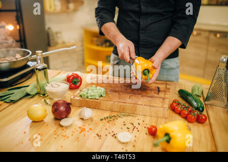 Chef with knife cuts yellow pepper on wooden board Stock Photo