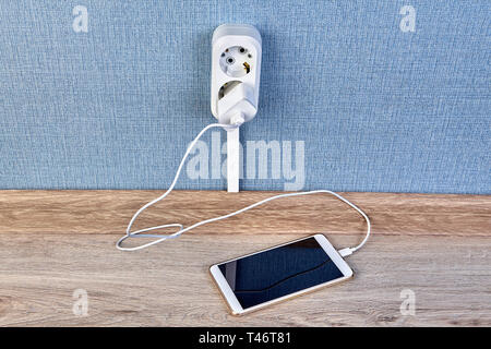 Charging  of smartphone with the charger and cable,  plugged into the electrical plug outlet. Stock Photo