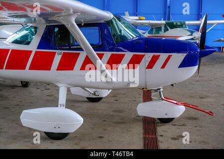 Small sport aircraft in hangar, side view, white, blue and red fuselage Stock Photo