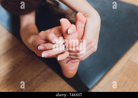 Close-up of a girl doing an asana bending forward with her hands towards her legs. Sitting on the floor on a pink yoga mat. Grip on foots. Marma