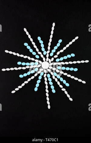 Snowflake made of white and blue pills on black background. Stock Photo