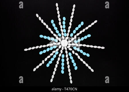 Snowflake made of white and blue pills on black background. Stock Photo