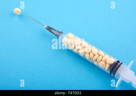 Syringe filled with yellow pills on blue background. Stock Photo