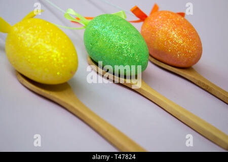 Colorful Easter eggs on pale pink background, egg in wooden spoons, green, orange, yellow, egg hunt decoration, selective focus
