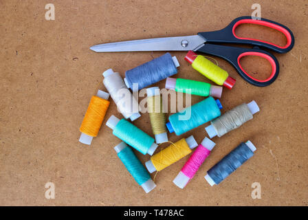 Multicolor sewing threads on a roll for sewing and tailoring scissors on a wooden background. With copy space Stock Photo