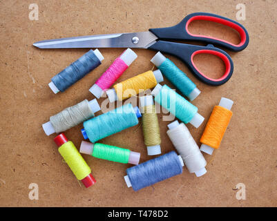 Multicolor sewing threads on a roll for sewing and tailoring scissors on a wooden background. With copy space Stock Photo