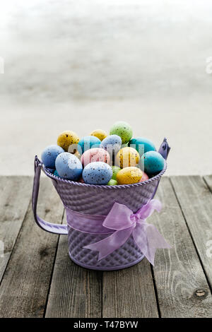 Easter eggs collected in a purple bucket with ribbon around, season holiday concept - Image Stock Photo