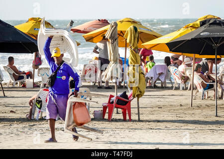 Cartagena Colombia,El Lagito,Hispanic resident,residents,man men male,Caribbean Sea public beach umbrellas carrying rental chairs,sand,COL190122154 Stock Photo