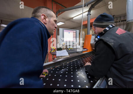 two young carpenters calculating and programming a cnc wood working machine in workshop. wood workers preparing a computer program for CNC machine at  Stock Photo