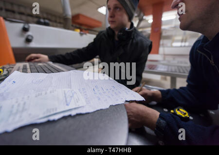 two young carpenters calculating and programming a cnc wood working machine in workshop. wood workers preparing a computer program for CNC machine at  Stock Photo