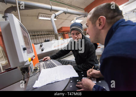 two young carpenters calculating and programming a cnc wood working machine in workshop. wood workers preparing a computer program for CNC machine at  Stock Photo