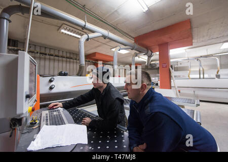 two young carpenters calculating and programming a cnc wood working machine in workshop. wood workers preparing a computer program for CNC machine at  Stock Photo