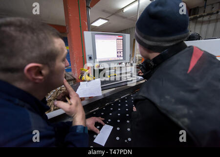 two young carpenters calculating and programming a cnc wood working machine in workshop. wood workers preparing a computer program for CNC machine at  Stock Photo