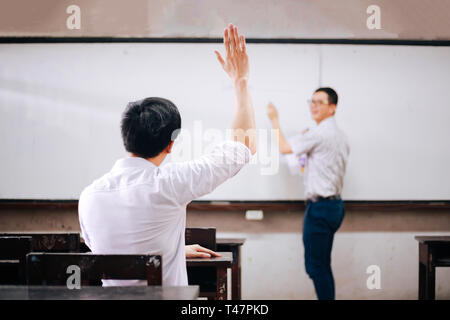 Young adult male student raising hands up in the air to ask questions from another male teacher Stock Photo