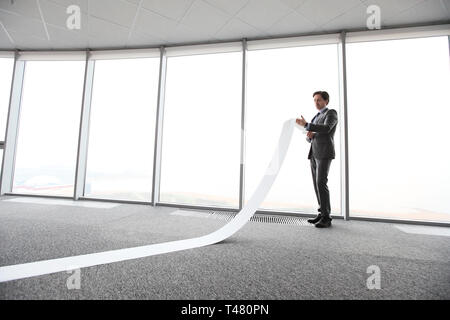 Businessman or male lawyer unrolling and reading long paper list in office Stock Photo