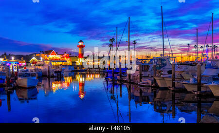 Oceanside harbor just after sunset with lighthouse and wharf lighted up, lights reflecting off the blue water and boats docked. Colorful sky. Stock Photo