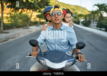 Parents with their little kid riding motorcycle on sunny city street Stock Photo