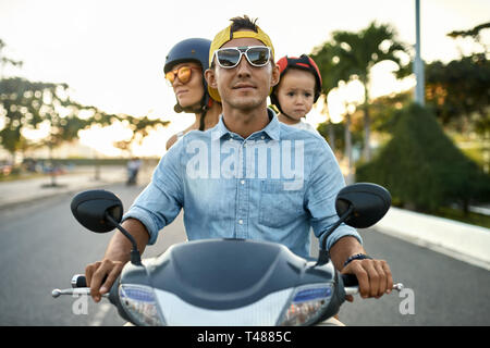 Parents with their little kid riding motorcycle on sunny city street Stock Photo