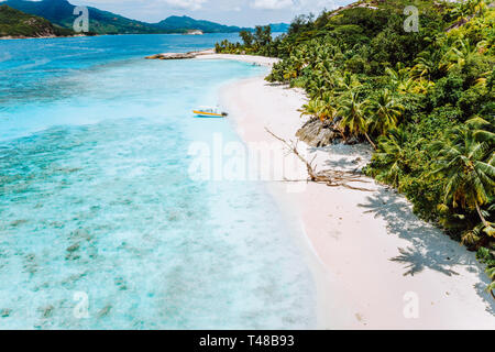 Daytrip to Therese Island. Mahe. A aerial drone view from blue lagoon and lonely tourist boat get ashore to sandy beach with tropical palm trees Stock Photo