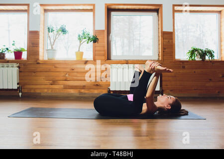 Young attractive woman practicing yoga, stretching in Ananda Balasana exercise, Happy Baby pose, working out, wearing black sportswear, cool urban Stock Photo
