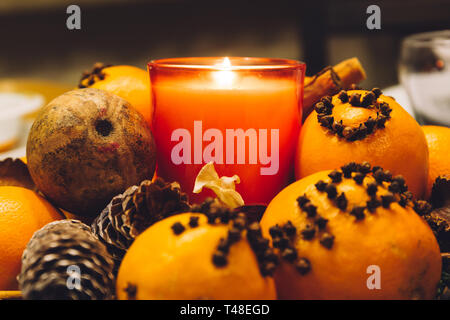 Christmas decoration candle set, with pine cones and oranges decorated with cloves, on a dinner table. Stock Photo