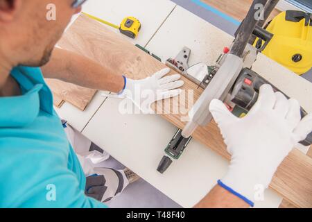 Caucasian Flooring Contractor at Work Cutting Piece of Laminate Panel Using Circular Table Saw. Stock Photo