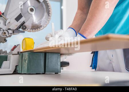 Contractor Worker Measuring Piece of Hardwood Before Cut Using Circular Saw. Construction Industry. Stock Photo