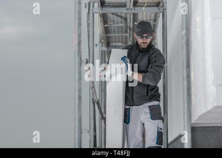 Caucasian Contractor Worker with Piece of Insulation Walking on a Scaffolding. Stock Photo