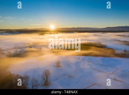 Sunrise over woods and meadows with morning fog in winter, at the back Alpine chain, near Geretsried, Tolzer Land, drone shot, Alpine foothills Stock Photo