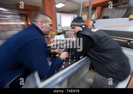 two young carpenters calculating and programming a cnc wood working machine in workshop. wood workers preparing a computer program for CNC machine at  Stock Photo