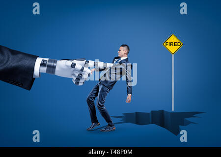 Big robotic hand pulling a businessman into earth crack with yellow FIRED sign on blue background Stock Photo