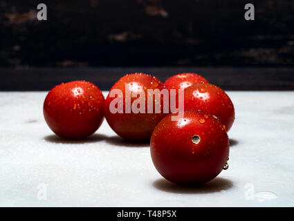 Five Cherry Tomatoes on a white marble table illuminated from above Stock Photo