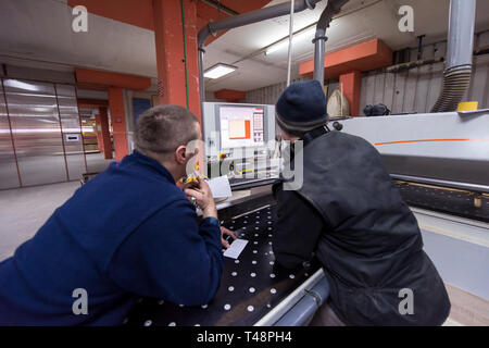 two young carpenters calculating and programming a cnc wood working machine in workshop. wood workers preparing a computer program for CNC machine at  Stock Photo
