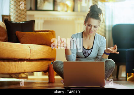 happy healthy sports woman in sport clothes at modern home watching yoga tutorial on internet via laptop. Stock Photo