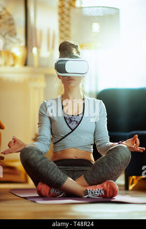 relaxed active woman in sport clothes at modern home doing yoga in VR gear. Stock Photo