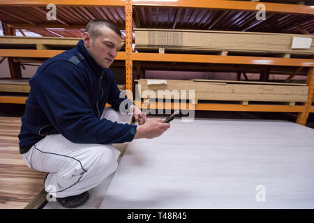 young man carpenter using a mobile phone to calculate measures for wooden board while working in big modern carpentry High quality wood concept Stock Photo