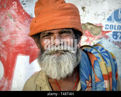 Elderly Indian beggar with a dirty orange turban headwrap poses for the camera. Stock Photo