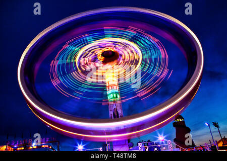 Long exposure image of a spinning fairground ride at night, painting vivid neon light trails that swirl into dynamic motion and thrilling lifestyle. Stock Photo