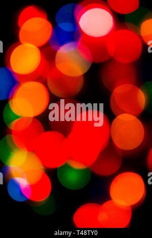 Softly blurred Christmas tree fairy lights glow in vibrant reds, greens, and golds, creating a warm, festive bokeh background of holiday magic. Stock Photo