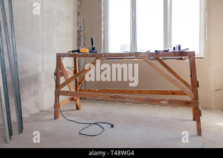Wooden scaffolding stand at the window in a large empty room, repair, plastering, painting walls, building tools, trash. Concept overhaul of the apart Stock Photo