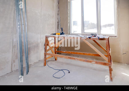Wooden scaffolding stand at the window in a large empty room, repair, plastering, painting walls, building tools, trash. Concept overhaul of the apart Stock Photo