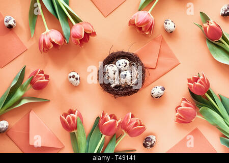 Easter flat lay on orange paper. Border made from Spring tulips, quail eggs, greeting cards and envelopes with bird nest in the middle. Stock Photo