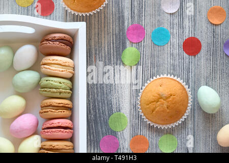 Spring celebration flat lay with macarons, muffins and marzipan eggs jn a decorative tray on textured grey wood Stock Photo