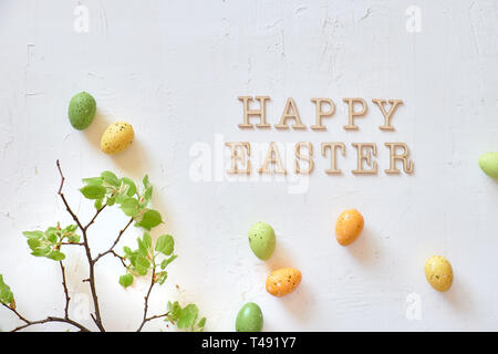 Fresh spring lime leaves, green and yellow decorative eggs and text "Happy Easter", flat lay on textured white background Stock Photo