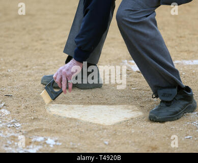 Umpire cleaning home plate at a baseball game Stock Photo