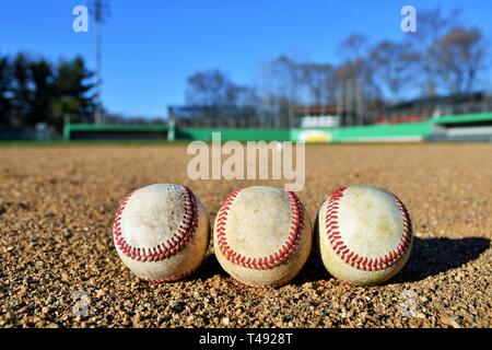 Photo of three game used baseballs on a baseball infield on a sunny day with a baseball field in the background Stock Photo