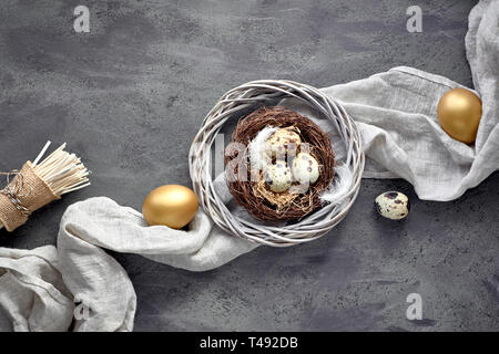 Easter flat lay on dark background with quail eggs in the nest, linen fabrique and two golden eggs on dark textured background Stock Photo