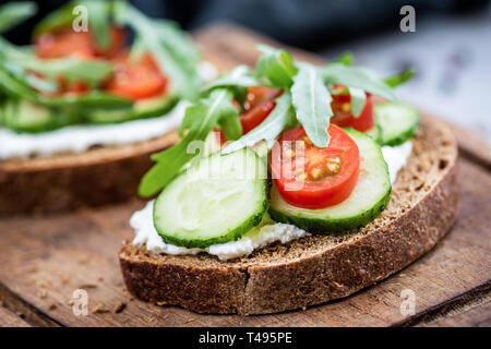Healthy food rye bread with cream cheese, cucumber, tomato and arugula. Closeup view Stock Photo