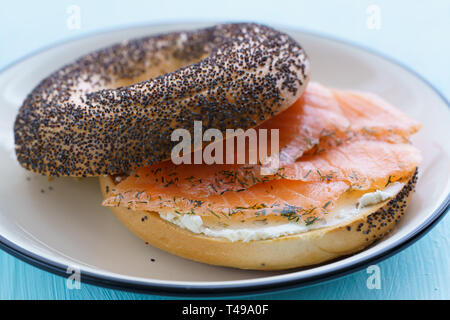 Poppy seeds bagel with cream cheese and smoked salmon served on a white plate with black rim. Blue table, high resolution Stock Photo