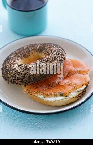 Poppy seeds bagel with cream cheese and smoked salmon served on a white plate with black rim. Blue table, high resolution Stock Photo